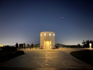 洛杉磯格里斐斯天文台（Griffith Observatory）夜晚景觀，簡約幾何結構的觀測塔在深藍夜色下發出柔和黃光，俯瞰城鎮燈火。
