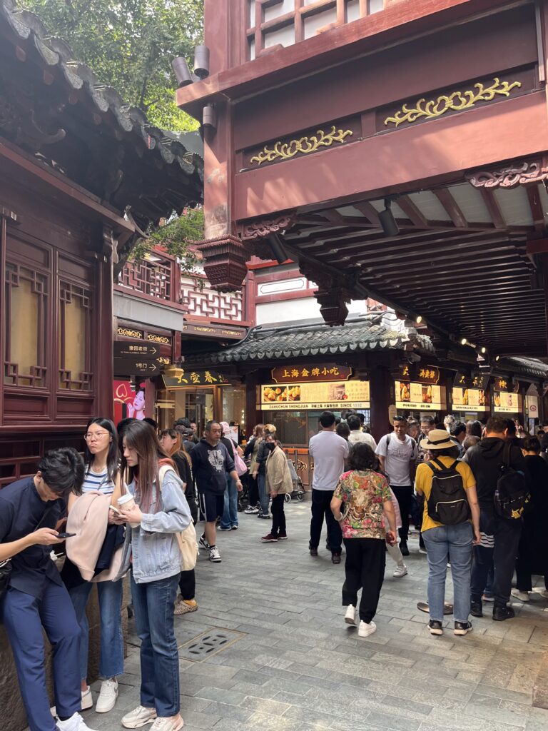 上海豫園老街街景，傳統中式建築林立，遊客穿梭於石板路與商店之間，呈現老城區熱鬧的日常氛圍