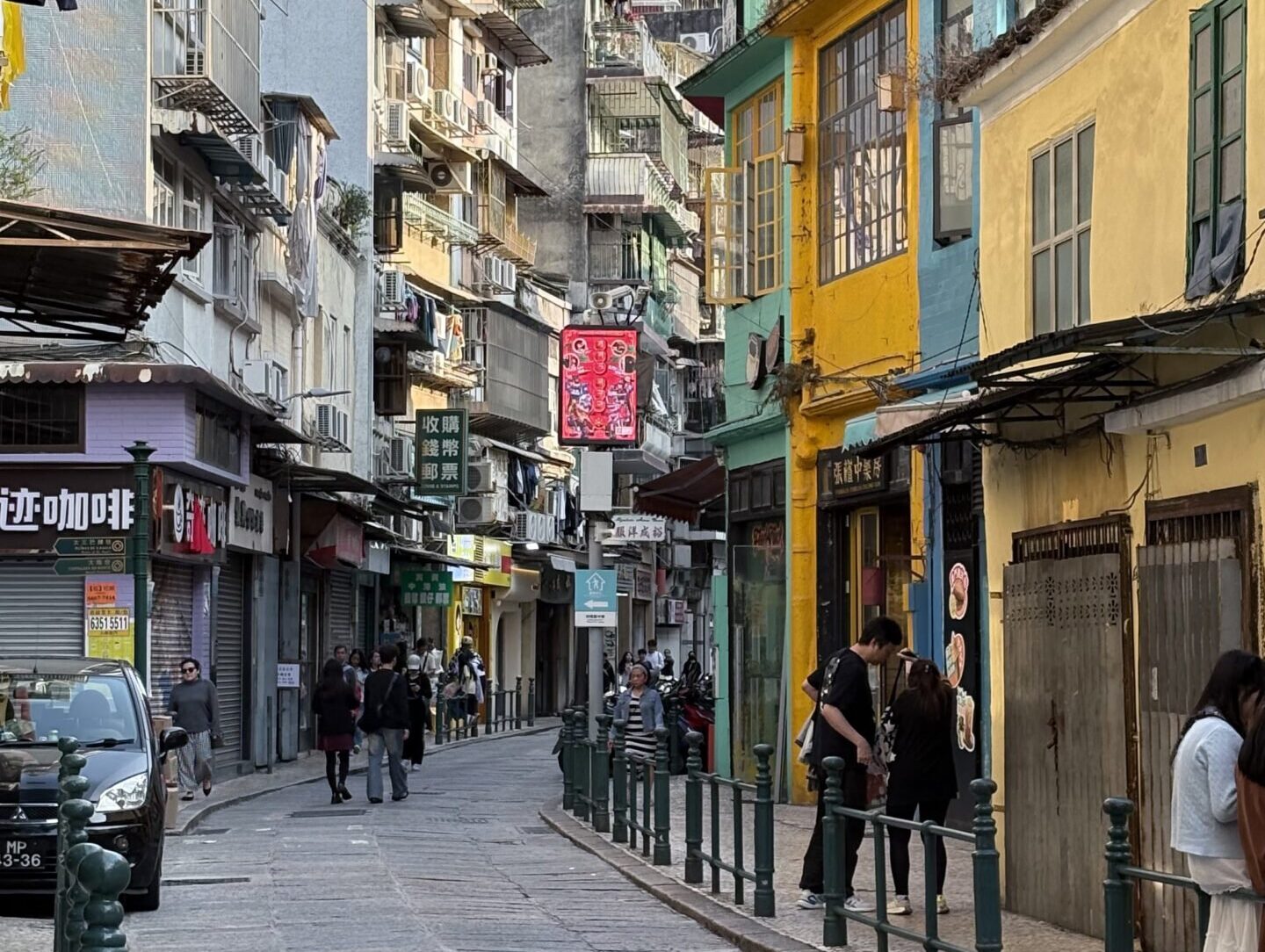 澳門舊城區彩色街屋與狹窄石板路，葡式建築立面交錯，呈現日常生活感的澳門街景