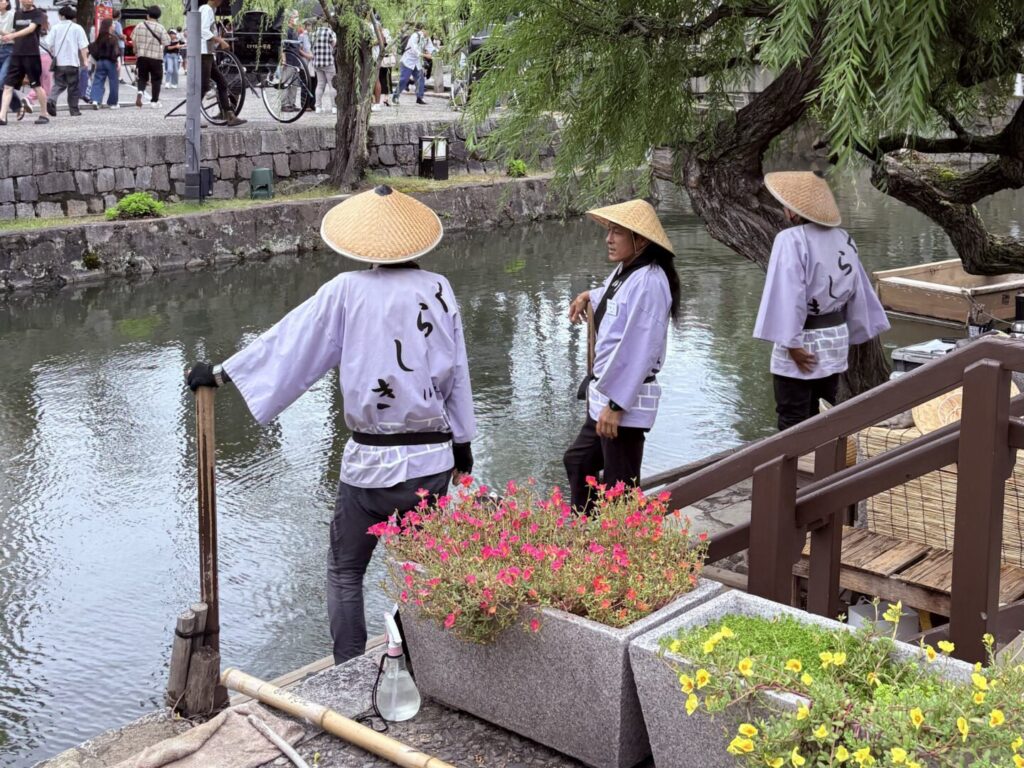 倉敷美觀地區|日本倉敷的 1 段散步旅遊記錄 日本岡山倉敷美觀地區,身穿傳統服裝、戴斗笠的船夫在柳樹下準備人力船,河岸旁擺放花盆與竹竿