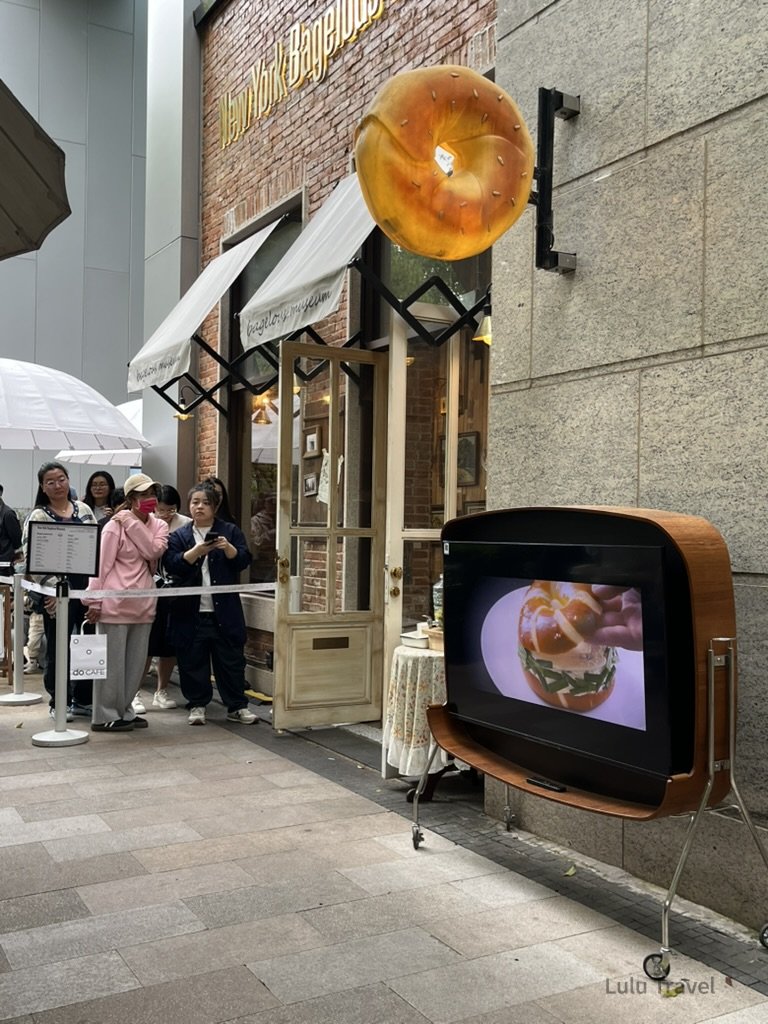 上海貝果博物館外觀，巨型貝果招牌懸掛於立面，店外排隊人潮等候入場
