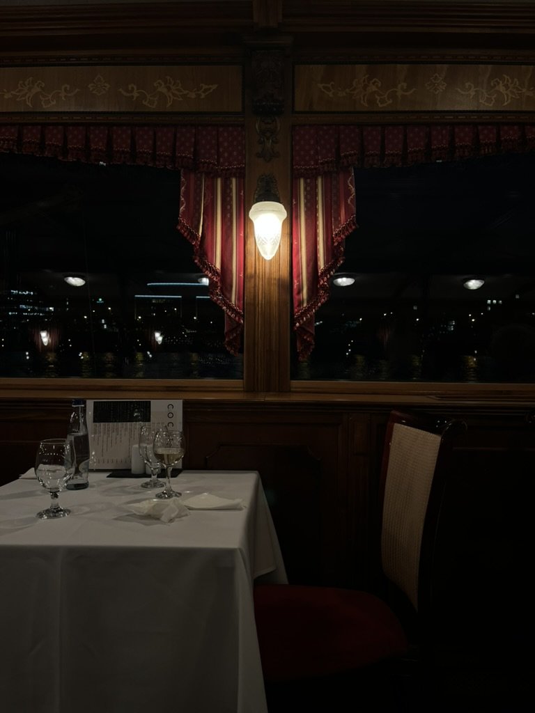 布達佩斯旅遊|第 1 次夜遊多瑙河 布達佩斯夜遊多瑙河晚宴特寫,精緻餐桌、紅色垂墜窗簾與古典壁燈,營造出華麗感十足的室內光影層次。