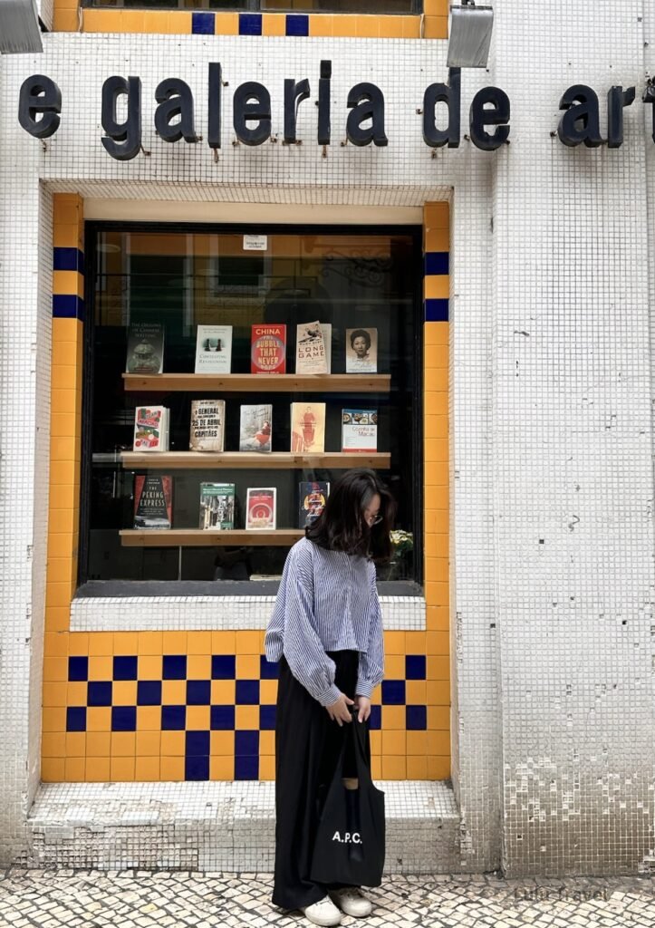 澳門葡文書局前的街景，女子站在葡式磁磚外牆與書店櫥窗前拍照，展現澳門中西文化融合的城市氛圍