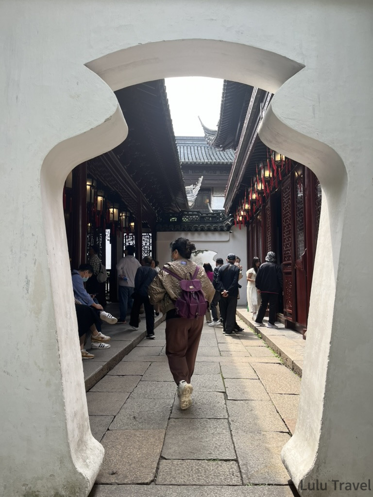 上海豫園的傳統中式花瓶門框景觀，遊客漫步在鋪著石板路與古典木造建築圍繞的庭園走道中。