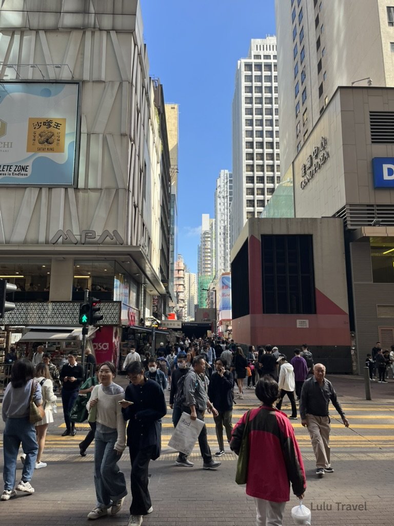 香港中環繁忙街景，行人穿越斑馬線，高樓林立的商業區呈現典型香港快節奏城市生活與街頭日常