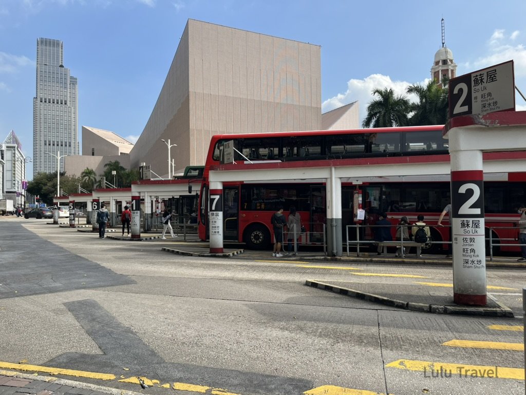 香港市區巴士總站實景，紅色雙層巴士停靠月台，背景可見現代建築與市中心街景，呈現香港旅遊行程第一站的交通與城市風貌