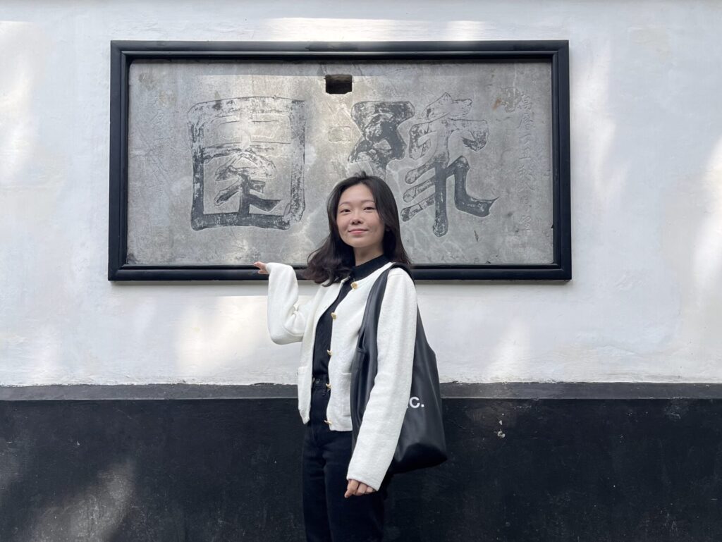 上海豫園園區內，一名旅人站在刻有「豫園」字樣的石碑前合影，背景為白牆與傳統中式園林建築