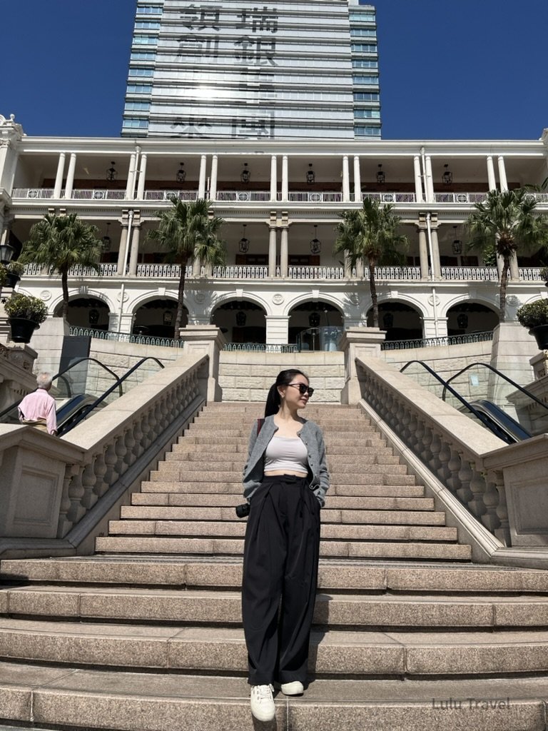 澳門城市街景，旅人站在階梯前，背景為歐式殖民風格建築與現代高樓並存的城市景觀
