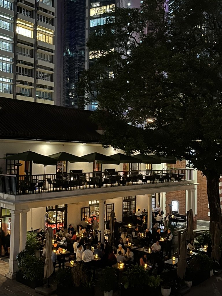 香港中環夜晚餐廳露台景色，戶外座位坐滿用餐人潮，背景為高樓林立的城市夜景，是下班後聚餐與旅遊推薦地點