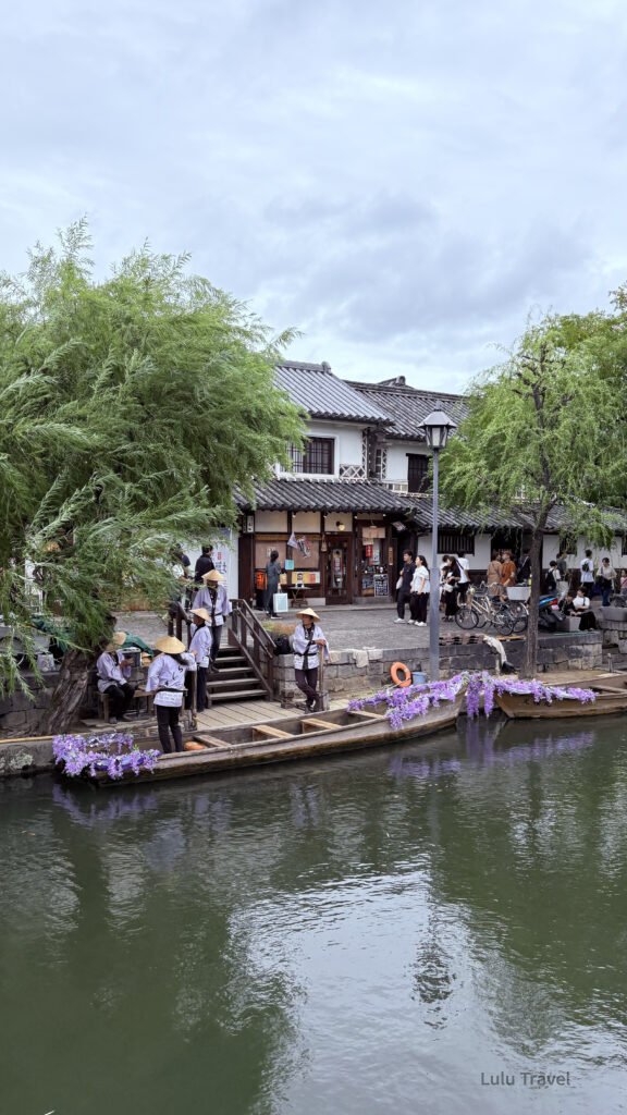Slow Travel in Japan Kurashiki: An Afternoon Without an Agenda 日本岡山倉敷美觀地區運河景色,柳樹下的遊船停靠岸邊,船夫穿著斗笠準備行程,周圍為傳統白牆町屋街景
