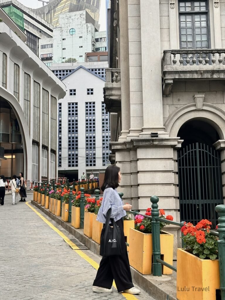 澳門街景隨拍，人物走在拱門建築旁的人行道，花槽與歐式建築形成城市日常風景