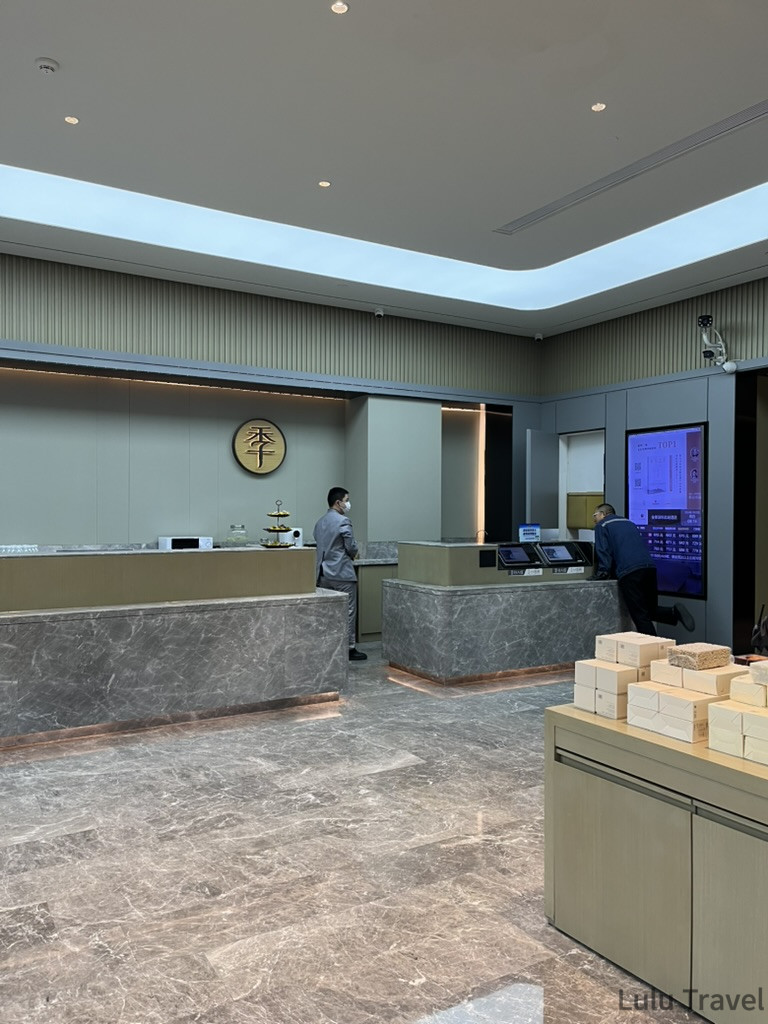 深圳出差住宿飯店大廳，現代簡約風格大理石地板與金色漢字品牌標誌，服務人員站在接待櫃台前