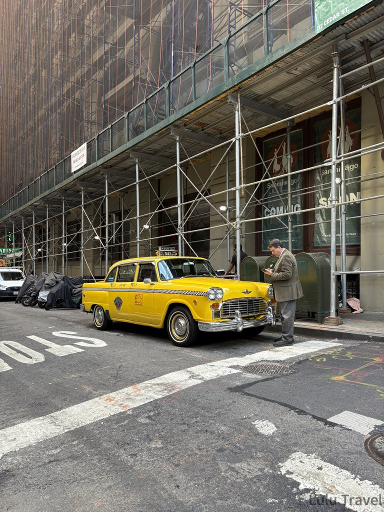 停靠在紐約街頭的復古黃色計程車（Checker Taxi），經典的車型與亮黃色車身與背景的施工鷹架形成鮮明對比。