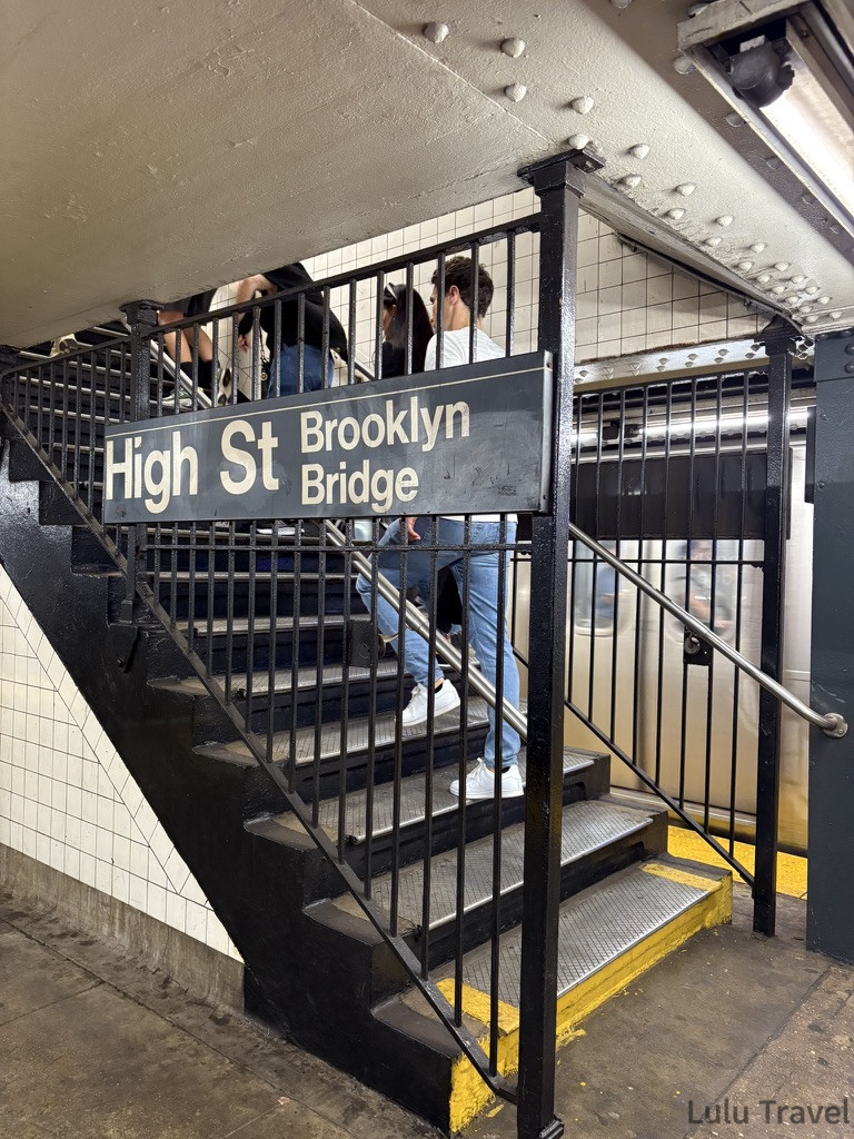 紐約地鐵 High St - Brooklyn Bridge 站出口階梯實況，標示牌明確導引前往布魯克林大橋方向，展現真實的車站內裝。