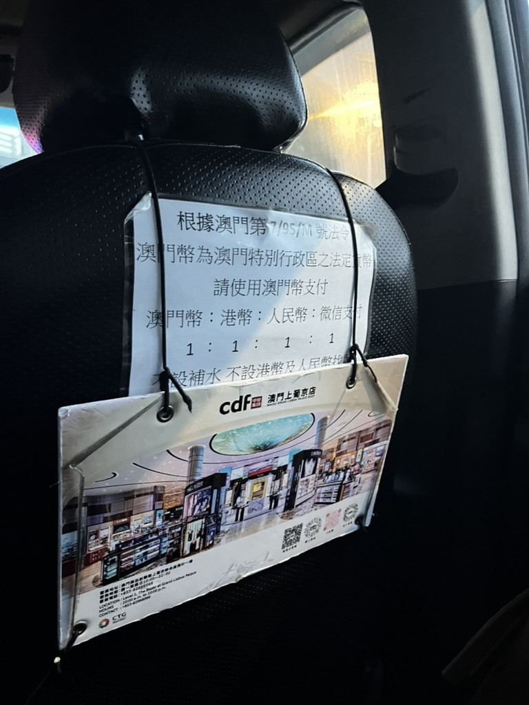 澳門計程車後座貼有澳門幣港幣人民幣匯率說明，旁附 CDF 澳門上葡京店廣告