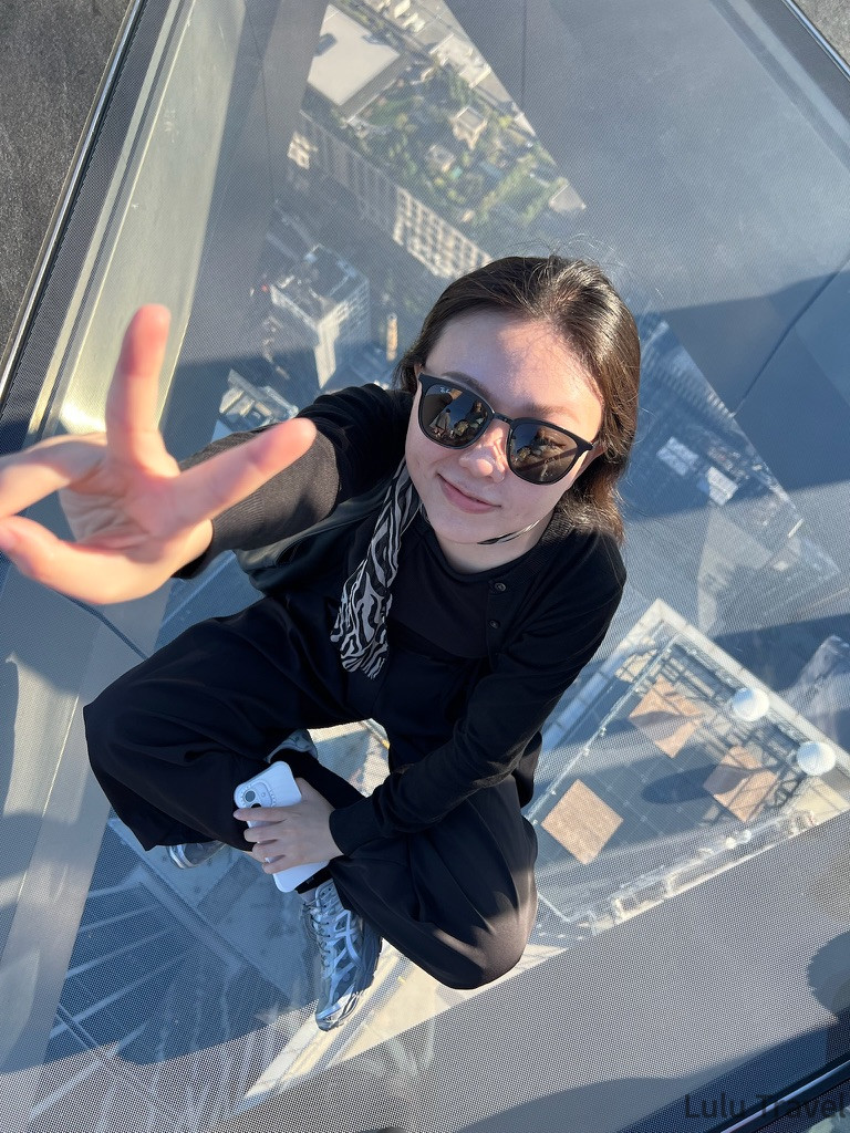 紐約行程規劃|DUMBO、百老匯、布魯克林到波士頓一日遊 旅客坐在 Edge 觀景台著名的角落透明玻璃地板上,從高空視角直接俯瞰下方的曼哈頓街區建築,展現極具衝擊力的城市高度與空間設計感。