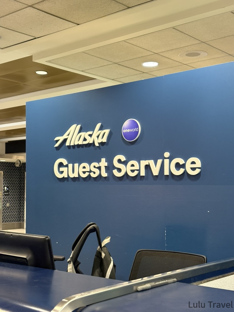 西雅圖機場內的阿拉斯加航空（Alaska Airlines）旅客服務櫃檯藍色牆面與 Guest Service 標誌特寫，是尋求班機延誤理賠與機票簽轉的核心地點。