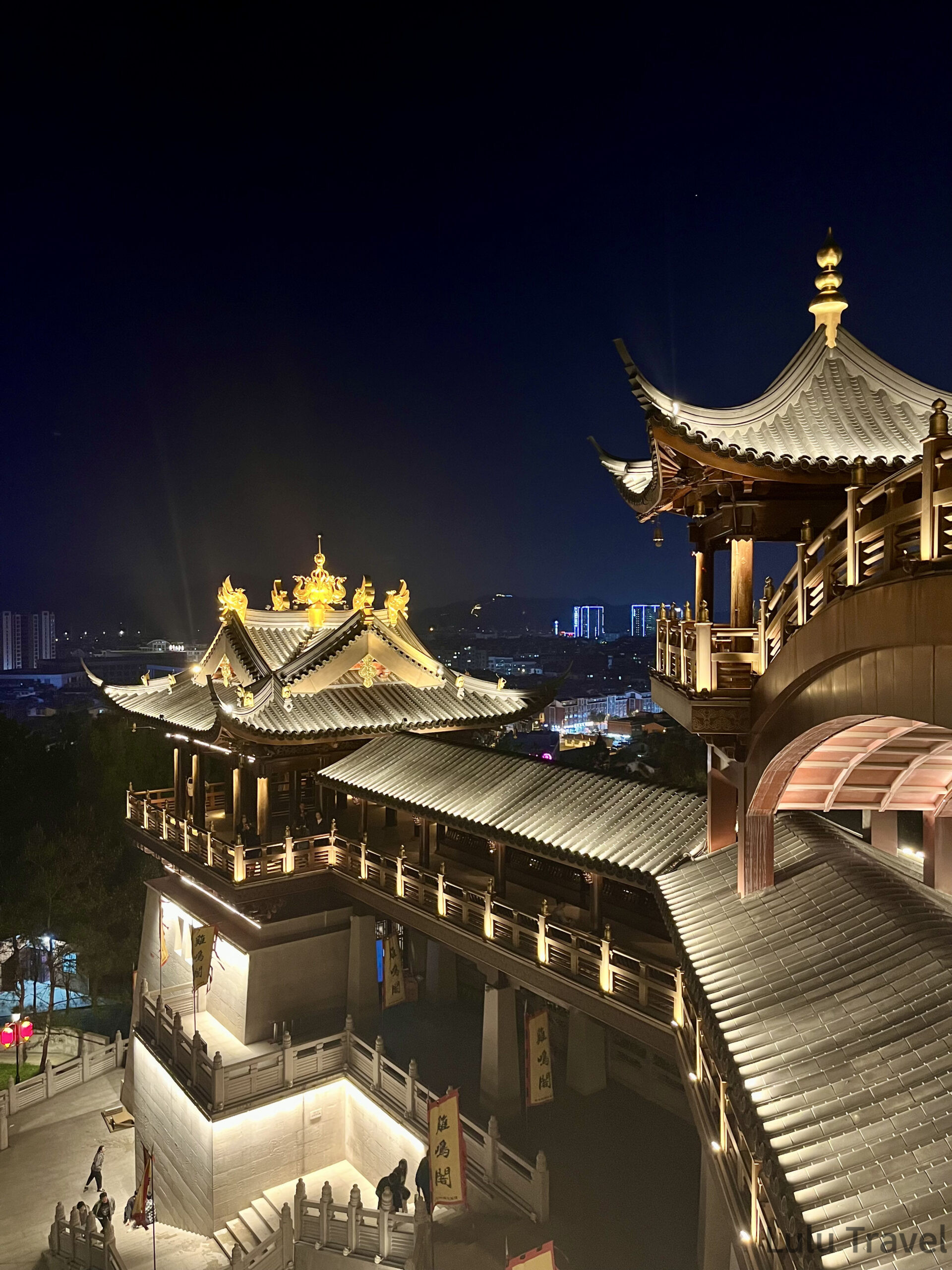 義烏雞鳴閣夜間高角度全景，金色鳳凰雕飾屋頂與多層傳統建築群在燈光下清晰可見，背景為義烏城市夜景