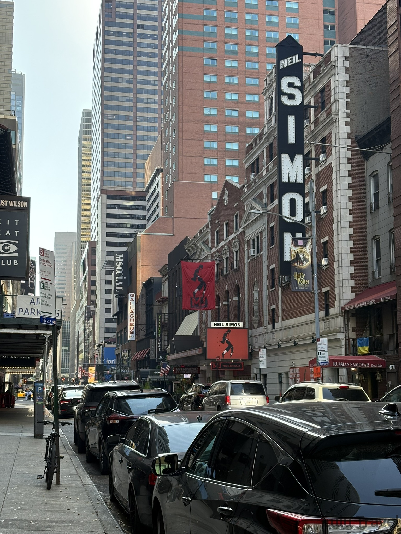 紐約百老匯 52 街街景，可見尼爾·西蒙劇院（Neil Simon Theatre）的大型垂直招牌，牆面上掛著《哈利波特與被詛咒的孩子》音樂劇旗幟與 MJ 音樂劇廣告。