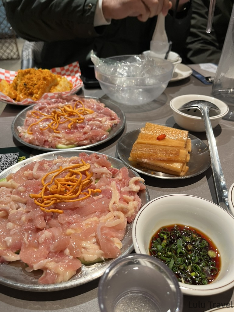 中國出差應酬飯局桌上的生豬肉火鍋食材，大盤薄切豬肉片搭配金針菇，旁附醬油蔥花沾醬與滷筍乾