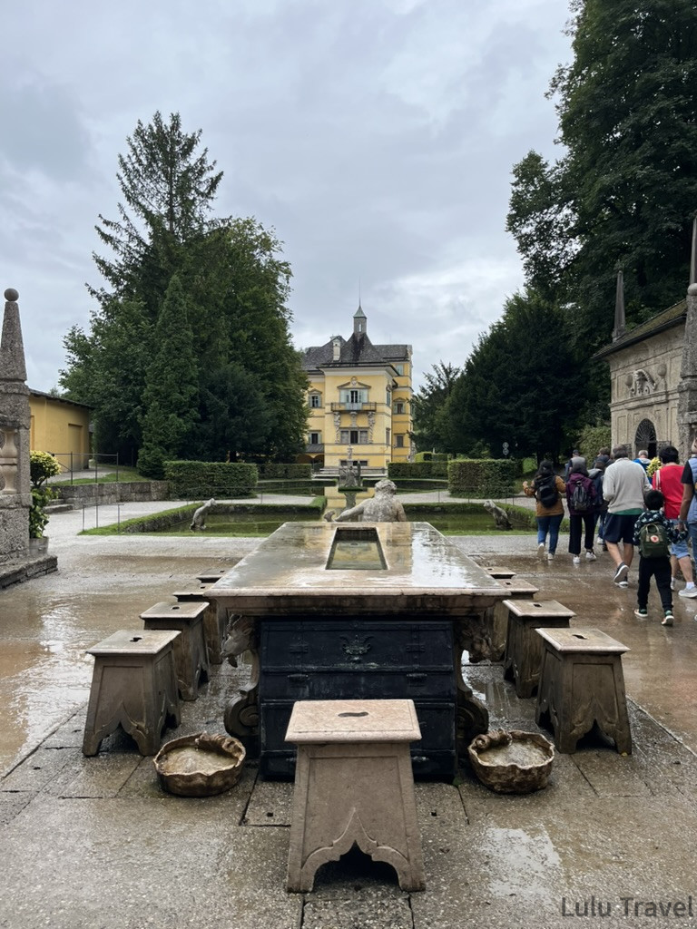 薩爾斯堡海爾布倫宮 Hellbrunn 水花園，前景為石桌噴水機關，背景為黃色巴洛克宮殿建築